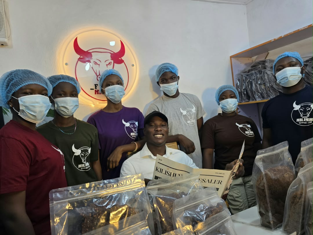 Feshitan with the Fesh Kilishi production team in hairnets and masks beside packed stock